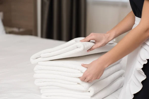 Corte tiro de empregada com pilha de toalhas limpas na cama na suíte do hotel — Fotografia de Stock