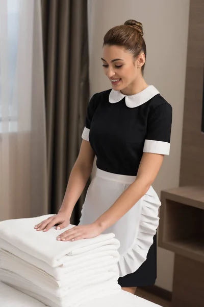 Young beautiful maid in uniform with stack of clean towels — Stock Photo