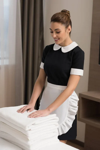 Joven hermosa criada en uniforme con pila de toallas limpias - foto de stock