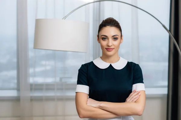 Young attractive maid in uniform with crossed arms at hotel suite — Stock Photo