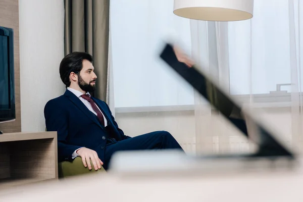 Hombre de negocios guapo sentado en sillón y mirando hacia otro lado - foto de stock