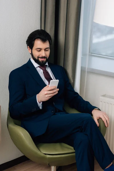 Hombre de negocios guapo usando teléfono inteligente mientras está sentado en el sillón - foto de stock