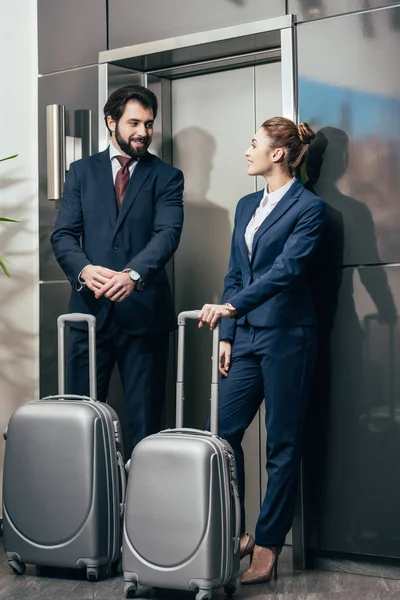 Jóvenes empresarios felices con el equipaje esperando ascensor juntos - foto de stock