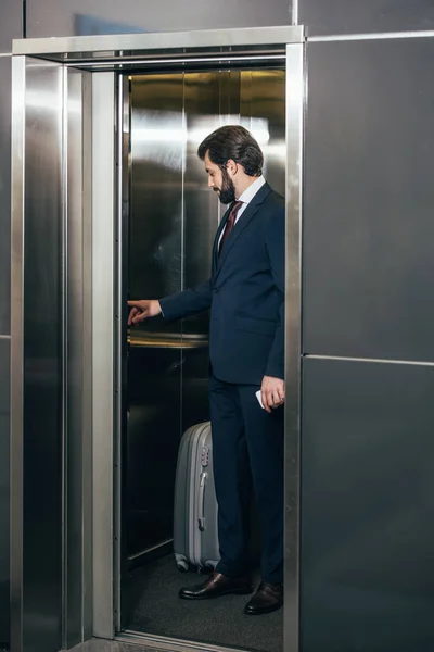 Homme d'affaires avec bagage appuyant sur le bouton à l'intérieur ascenseur — Photo de stock
