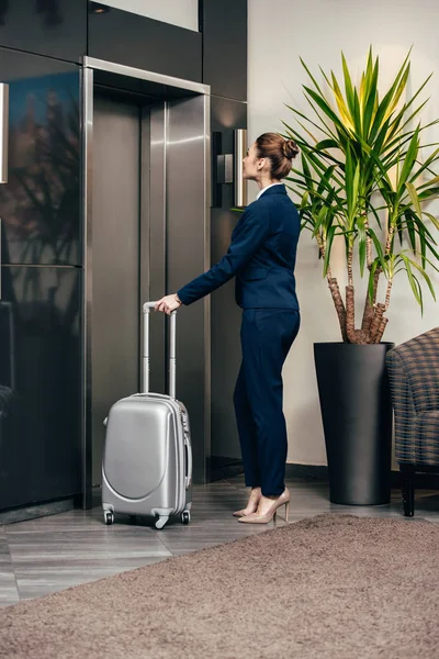 Young attractive businesswoman waiting for elevator at hotel with luggage — Stock Photo