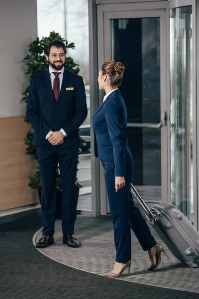 Businesswoman going out of hotel luggage and looking at doorman — Stock Photo