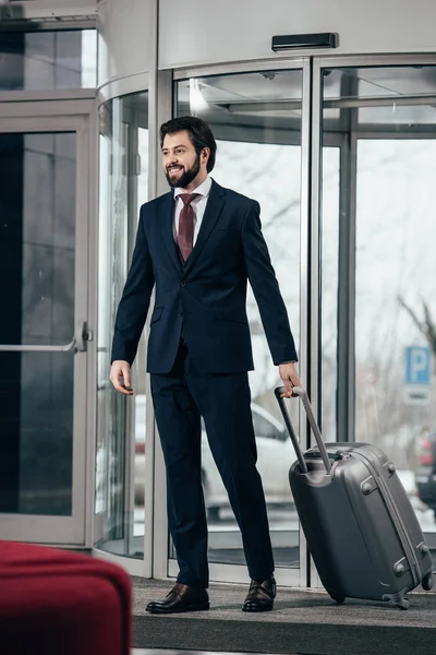 Hombre de negocios guapo con equipaje saliendo del hotel - foto de stock