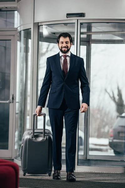 Feliz hombre de negocios guapo con el equipaje que sale del hotel - foto de stock