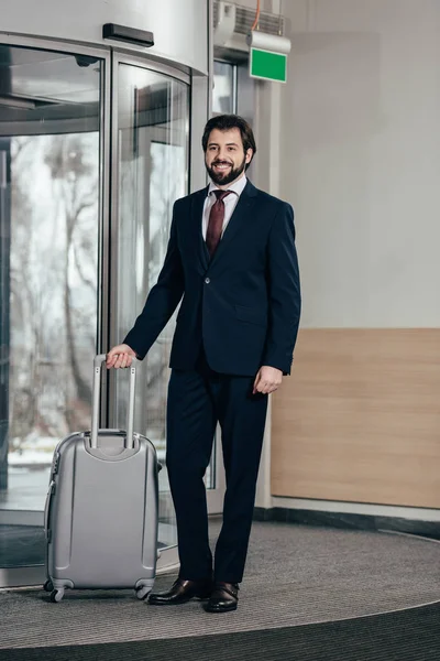 Homem de negócios bonito sorridente com bagagem saindo do hotel — Fotografia de Stock
