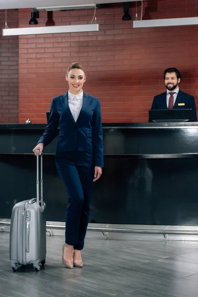 Femme d'affaires attrayante avec des bagages debout devant le comptoir de réception de l'hôtel avec administrateur — Photo de stock