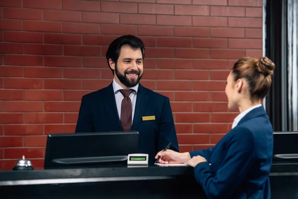 Receptionist hotel parlando con il cliente mentre lei firma il contratto al bancone — Foto stock