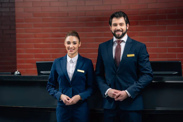 Hotel receptionists standing together in front of counter and looking at camera — Stock Photo
