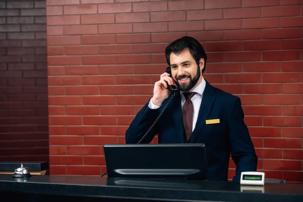 Recepcionista sonriente del hotel atendiendo llamadas telefónicas en el lugar de trabajo - foto de stock