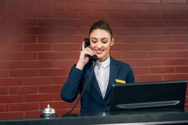 Joven hermosa recepcionista del hotel recibiendo llamada en el lugar de trabajo - foto de stock