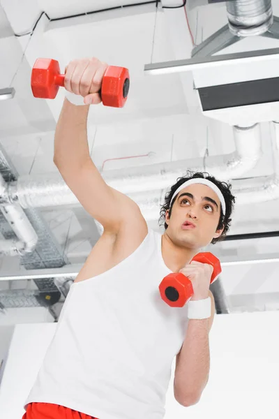 Visão de baixo ângulo do jovem magro exercitando com halteres — Fotografia de Stock