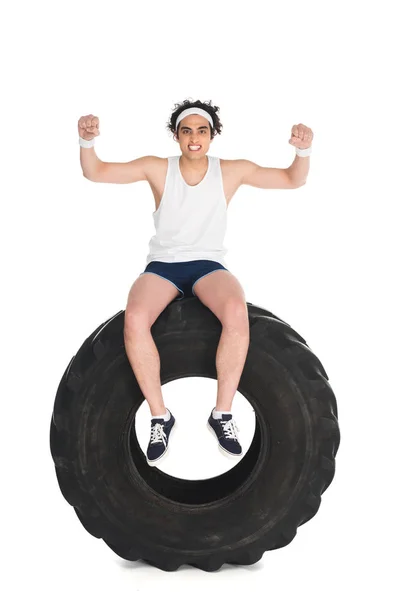 Exult thin sportsman sitting on tire of wheel isolated on white — Stock Photo