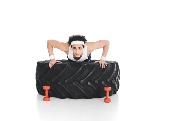 Young thin sportsman doing push ups on tire of wheel isolated on white — Stock Photo