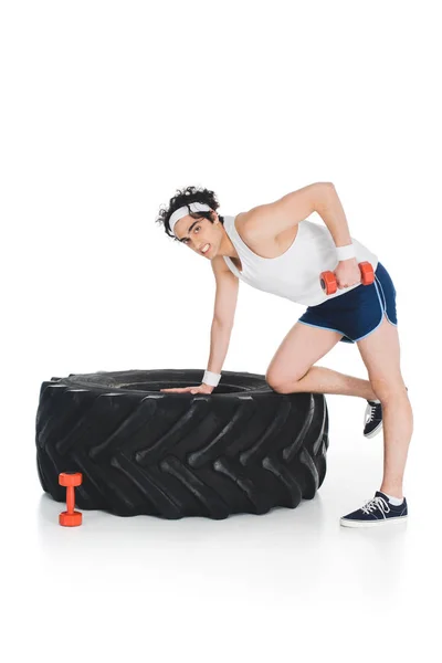 Sportsman thin exercising with dumbbell near tire of wheel isolated on white — Stock Photo