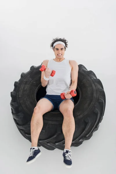 High angle view of thin sportsman exercising with dumbbells inside tire of wheel isolated on white — Stock Photo