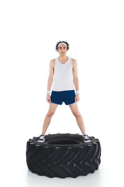 Young thin sportsman standing on tire of wheel isolated on white — Stock Photo