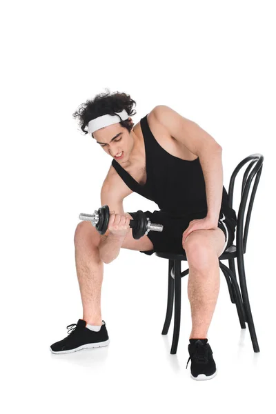 Молодой худой спортсмен упражняется с гантели, сидя на стуле изолированы на белом — стоковое фото