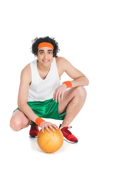 Улыбающийся тощий баскетболист сидит с мячом, изолированным на белом — стоковое фото