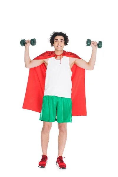 Deportista flaco sonriente con mancuernas de pie en capa roja aisladas en blanco - foto de stock