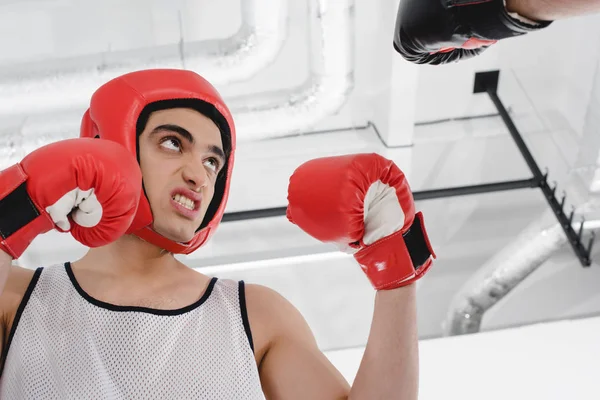 Vista de bajo ángulo del deportista flaco enojado en casco de boxeo y guantes - foto de stock