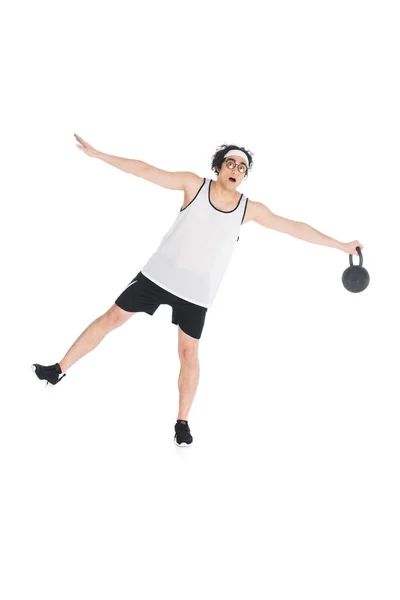 Young skinny sportsman in eyeglasses standing on one leg and holding kettlebell isolated on white — Stock Photo