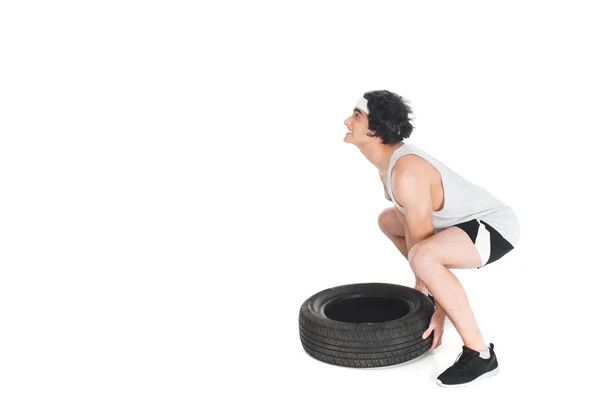 Side view of skinny sportsman raising tire isolated on white — Stock Photo