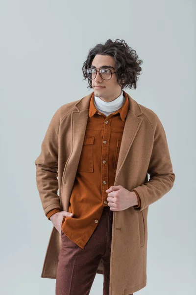 Joven hombre con estilo en gafas de pie con la mano en el bolsillo aislado en gris - foto de stock