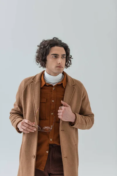 Joven hombre elegante con gafas en la mano aislado en gris - foto de stock