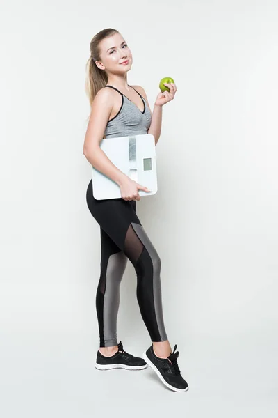 Молодая женщина в спортивном топе держит яблоко и чешуи изолированы на белом — стоковое фото