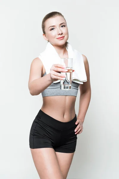 Blonde woman in sport clothes with towel on shoulders holding glass of water isolated on white — Stock Photo