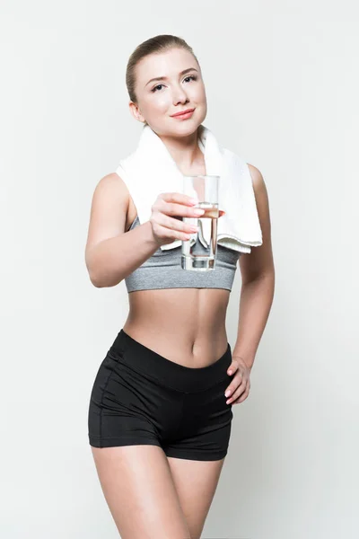 Mujer rubia en ropa deportiva con toalla sobre hombros sosteniendo vaso de agua aislado en blanco - foto de stock