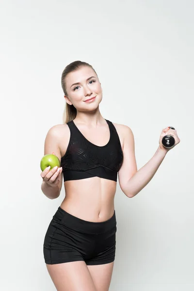 Young woman in sports top holding dumbbell and apple isolated on white — Stock Photo