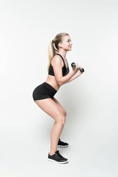 Attractive sportive girl performing squat with dumbbells isolated on white — Stock Photo