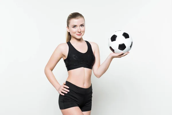 Sonriente mujer fitness sosteniendo pelota de fútbol aislado en blanco - foto de stock