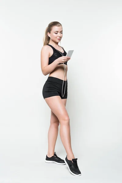 Sorrindo mulher fitness ouvir música no smartphone isolado no branco — Fotografia de Stock