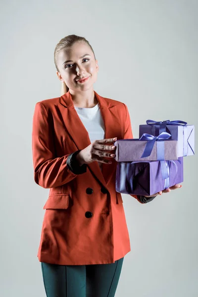 Smiling young woman holding gift boxes isolated on grey — Stock Photo