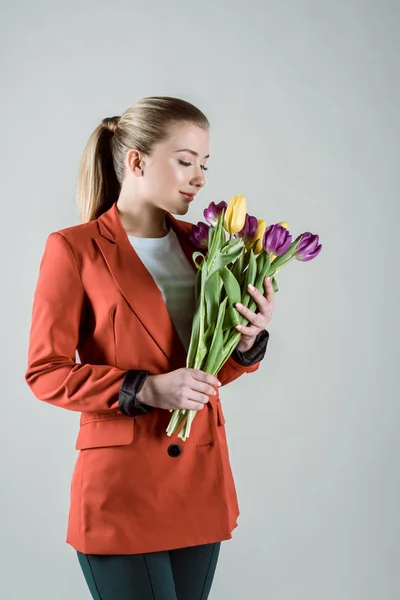 Chica atractiva oliendo tulipanes de primavera aislados en gris - foto de stock