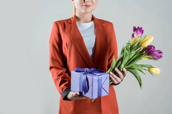 Geschenkbox und Tulpenstrauß in den Händen der stilvollen Frau isoliert auf grau — Stockfoto