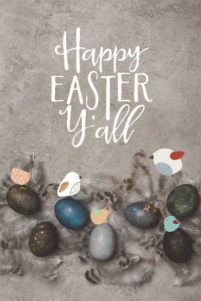 Top view of painted easter eggs with feathers on concrete surface with birds and Happy Easter you all lettering — Stock Photo