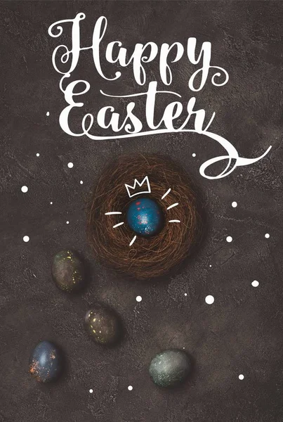 Top view of blue easter egg with crown in nest on concrete table with Happy Easter lettering — Stock Photo