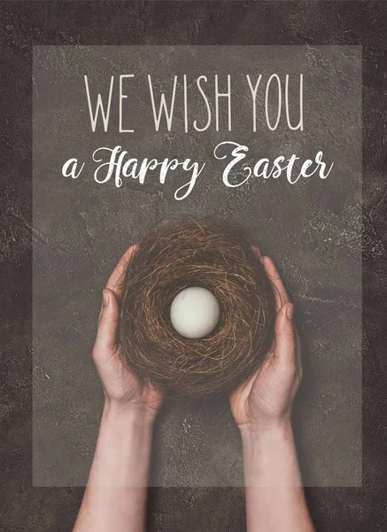 Vista recortada del hombre sosteniendo el nido con huevo blanco, y le deseamos una letra feliz de Pascua - foto de stock