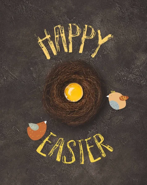 Top view of broken egg with yolk in nest on concrete surface with birds and Happy Easter lettering — Stock Photo