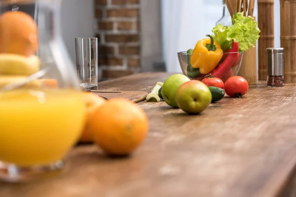 Selective focus of orange juice in glass jug, fresh fruits and vegetables on kitchen table — Stock Photo
