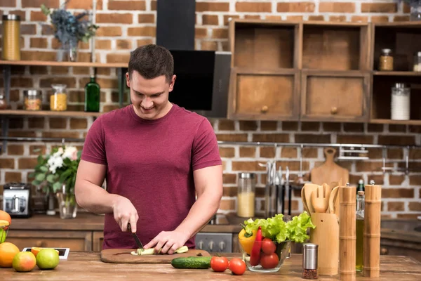 Lächelnder junger Mann schneidet Sellerie, während er Salat in der Küche kocht — Stockfoto