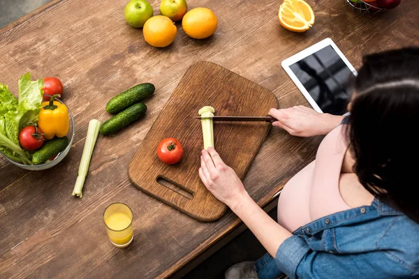 Обрезанный снимок молодой беременной женщины, режущей сельдерей во время приготовления пищи на кухне — стоковое фото