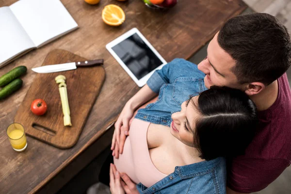 Vista aérea de la feliz joven pareja embarazada abrazando mientras cocinan juntos - foto de stock